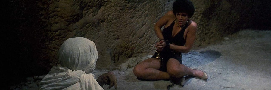 A creature approaches a woman in chains who looks at it with fear.