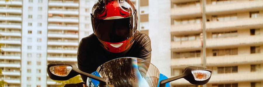 Someone in a motorbike helmet watches the street with apartment blocks behind.