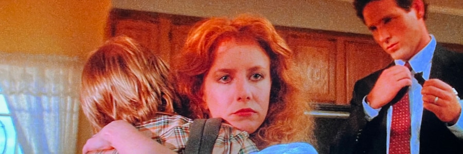 A woman holds her son and looks disconnected over his shoulder.
