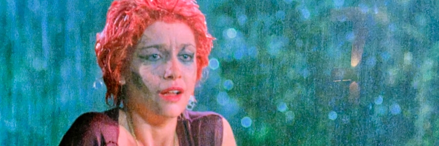 A woman shivering in a graveyard in the rain.