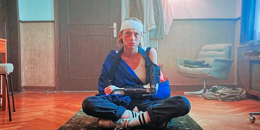 A woman sits cross-legged on the floor with her arm in a cast and a bandage around her head.