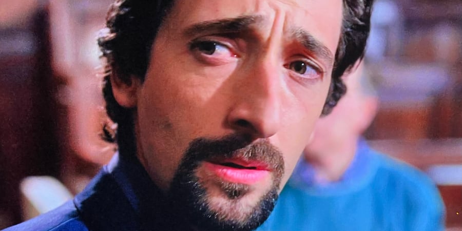 A detective with a goatee looks behind at something.
