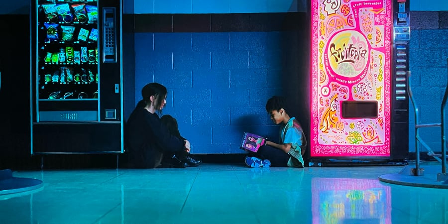 A boy and a girl sit across from each other and talk about a book the boy is holding.