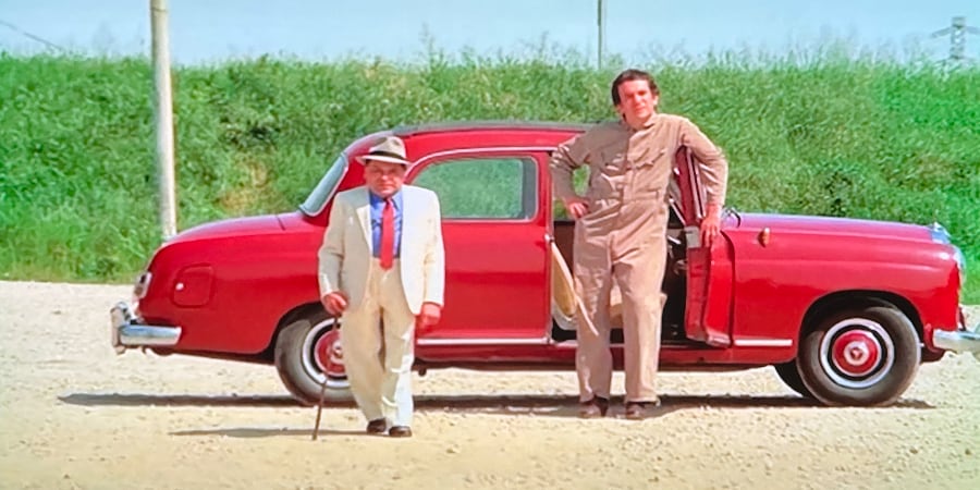 Two men with a red car await the arrival of a ferry.