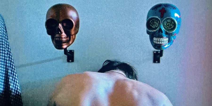 Two skulls grin from a wall over the shoulders of ayoung man.