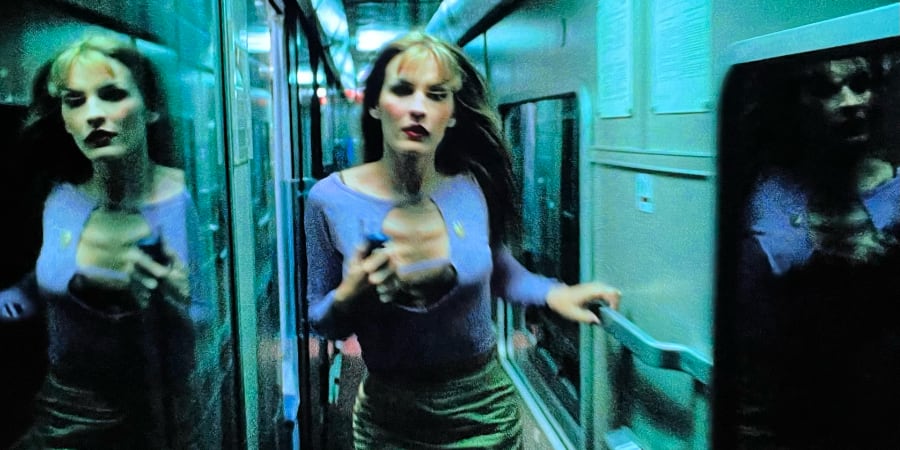 A frightened woman stumbles down an empty train corridor.