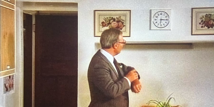 A man looks at his watch and checks the time against the wall clock.