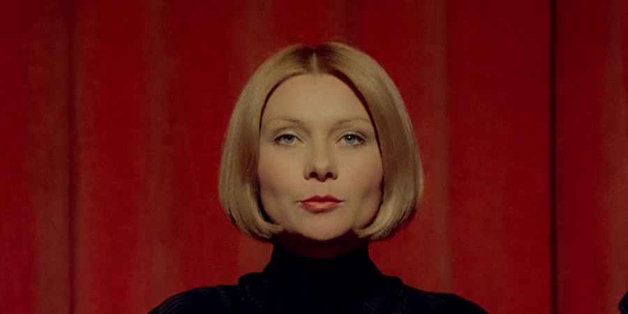 A woman stares out from a stage with a red curtain behind.