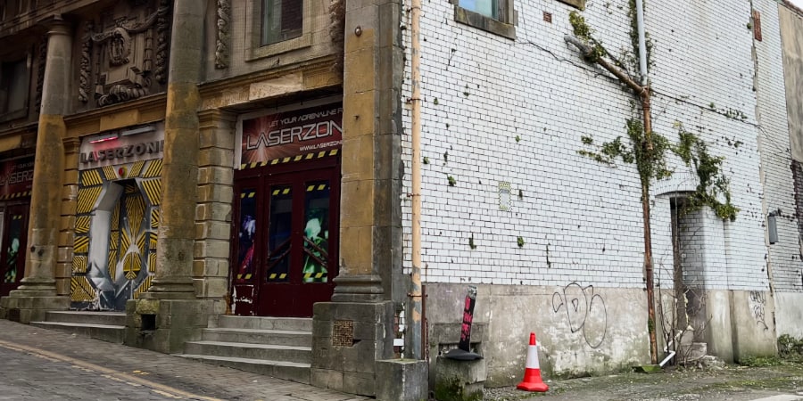 The corner of a brown brick old cinema and a painted white brick wall with an interesting mix of guttering and vines.