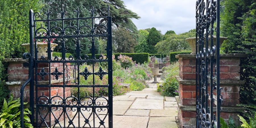 Black gates opening into an ornate country garden.