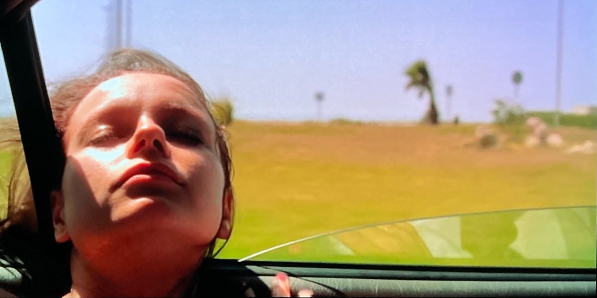 A woman hangs her head out of a moving car and looks peaceful.