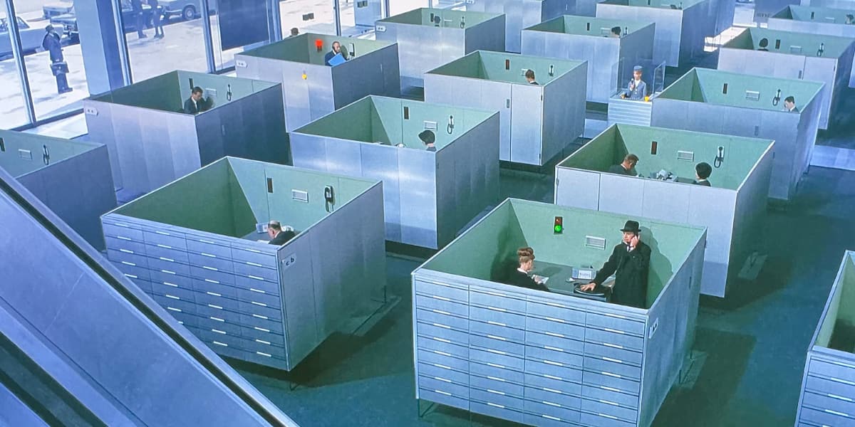 An office constructed from grey boxes each containing people doing business.
