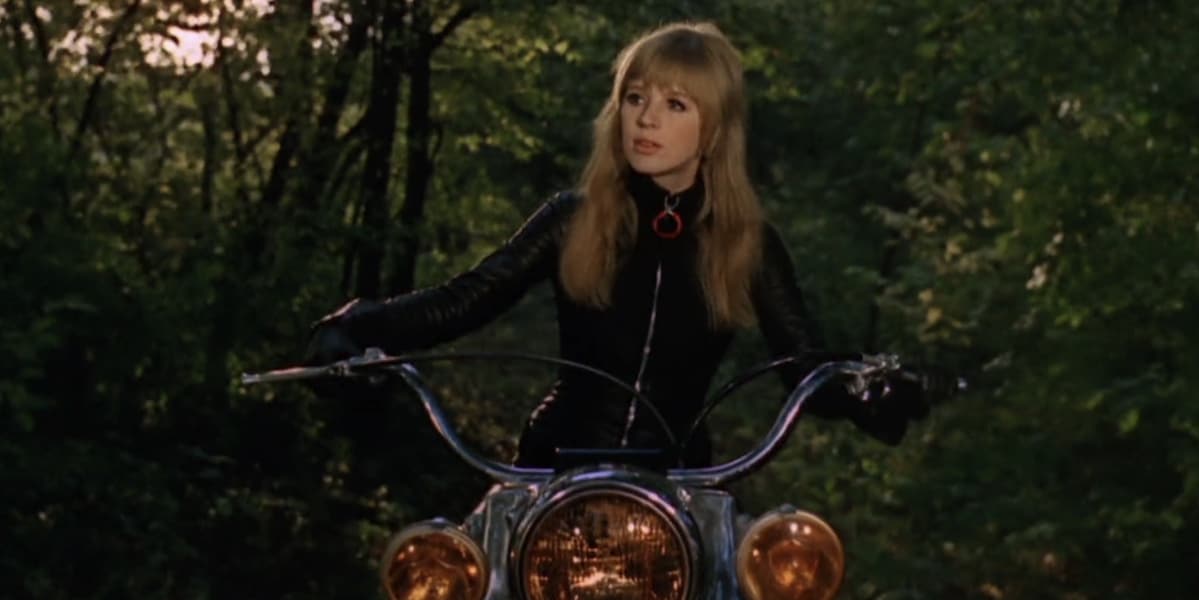 A woman in black biking leathers sits on a big black motorbike.