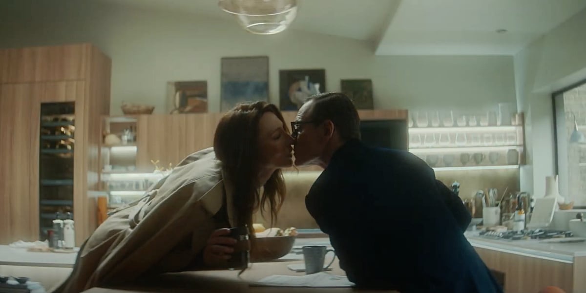 George and Kathryn reach to kiss across the kitchen table.