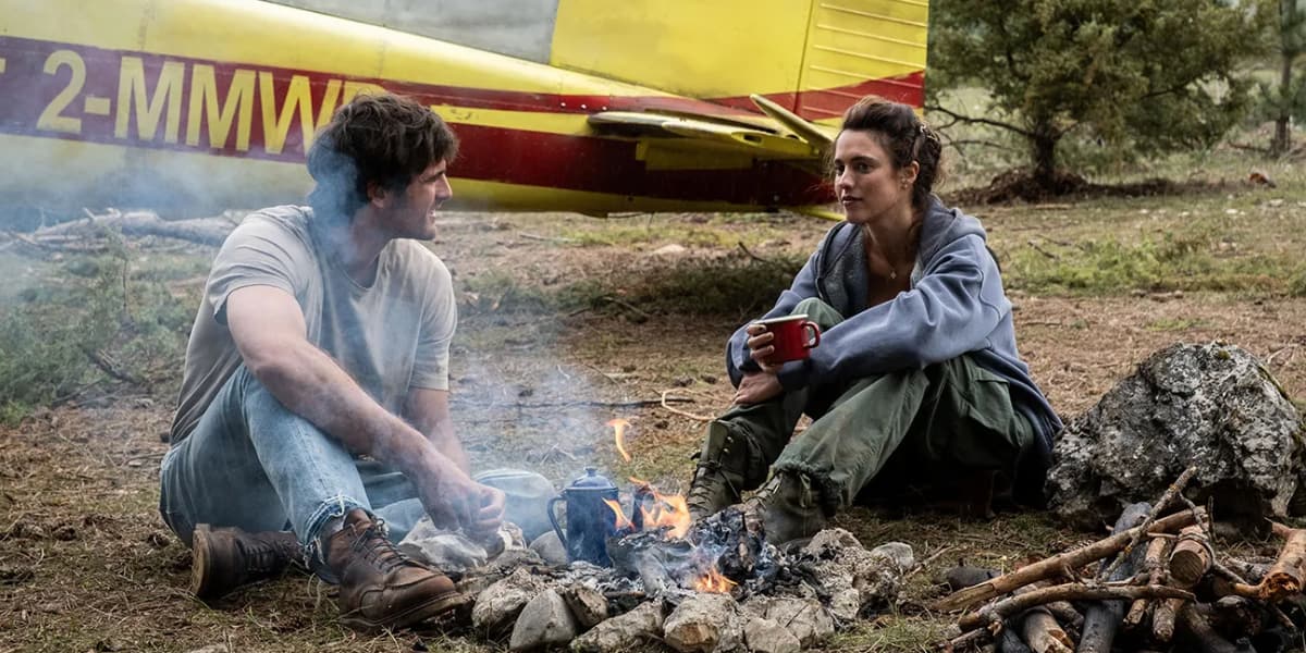 A man and a woman talk at a campfire.