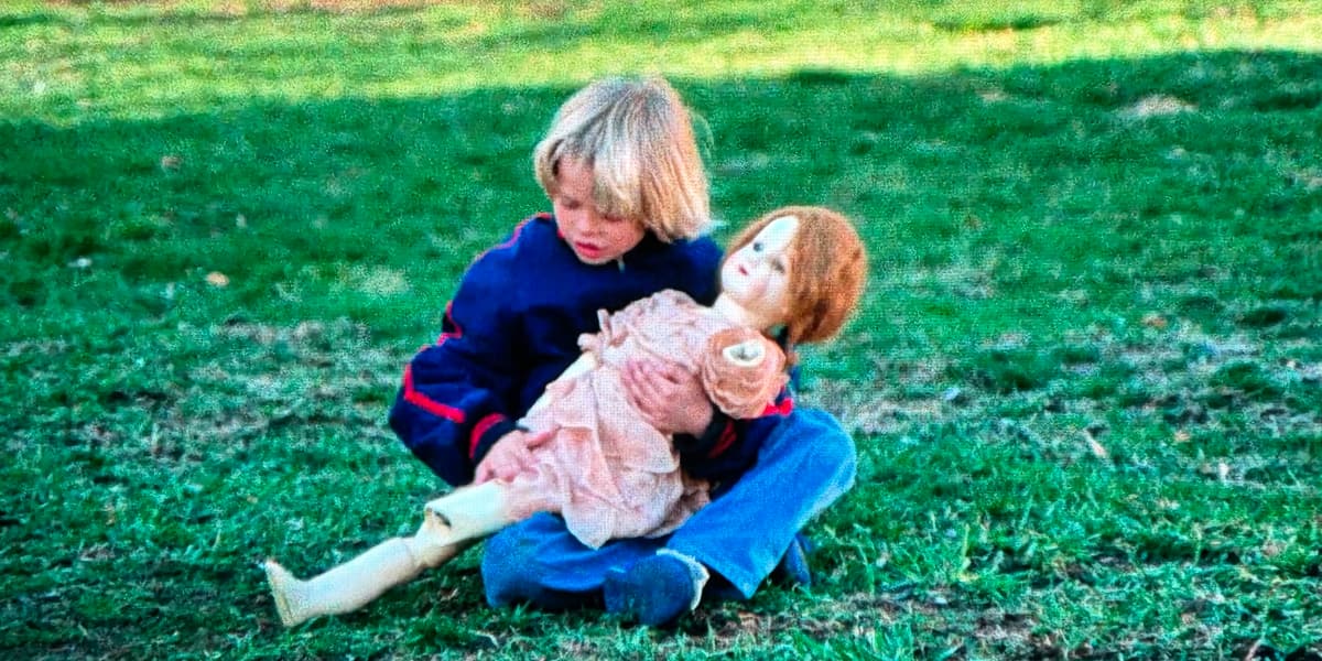 A boy sits on the grass cradling a one-armed doll.